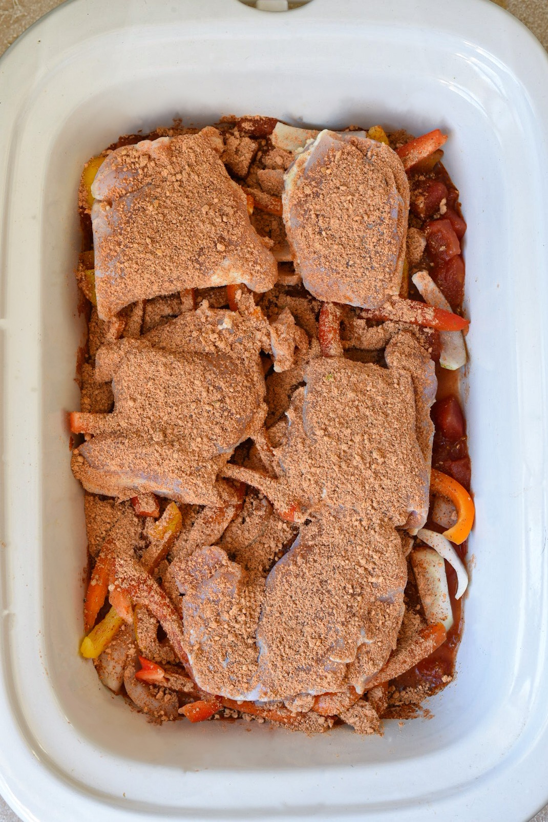 Raw chicken thighs in a slow cooker topped with spices