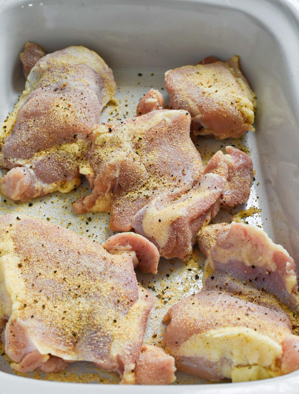 Raw chicken thighs in a slow cooker seasoned with spices and fresh cracked black pepper