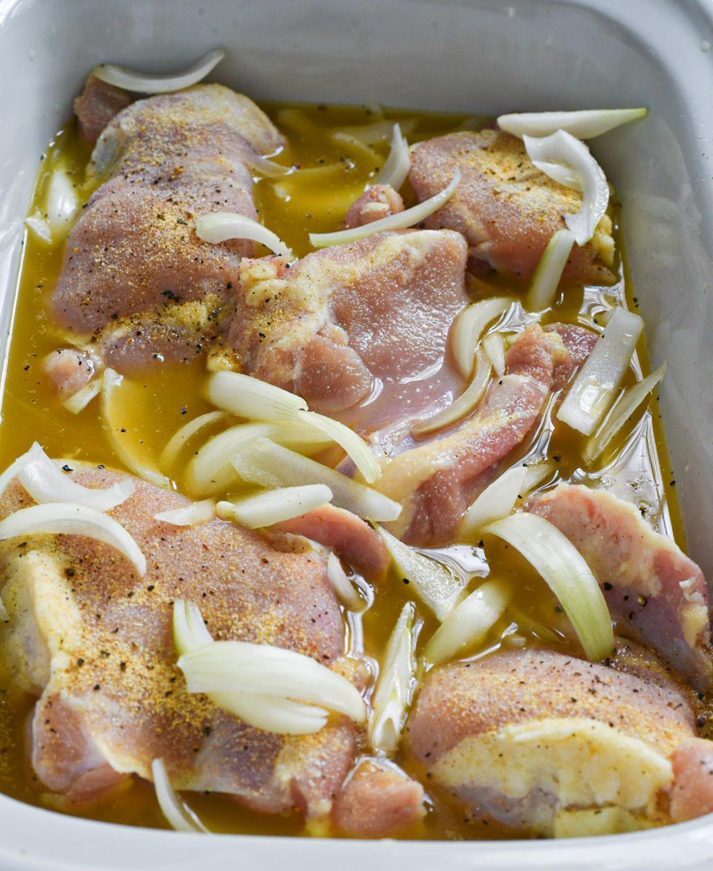 Raw chicken in a slow cooker topped with onion slices and surrounded by lemon chicken broth