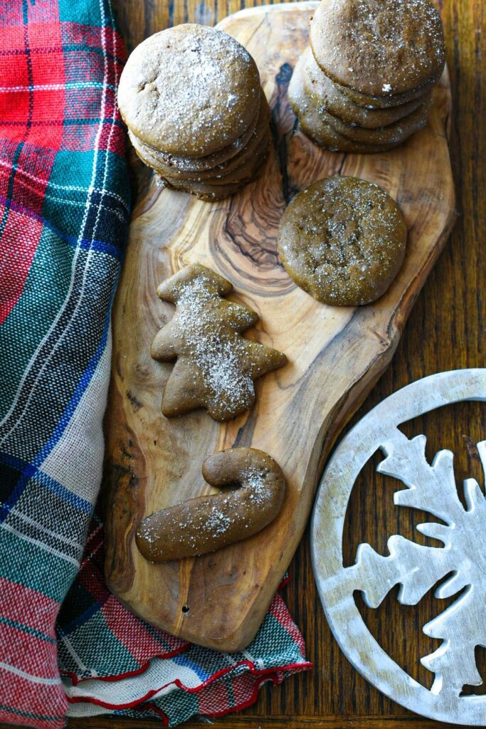 Gingersnap cookies in the shape of christmas cookies on a wooden serving board with a plaid blanket.