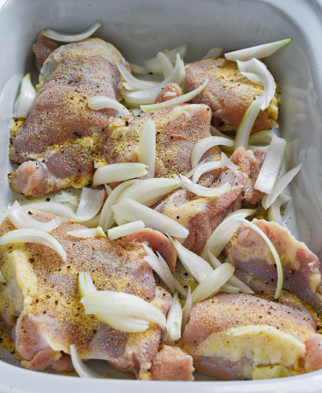 Raw chicken in a slow cooker seasoned and topped with raw onion slices