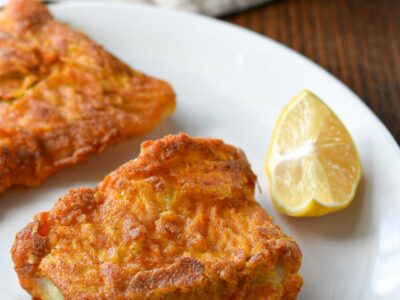 Baked scrod filets on a white plate with a cast iron skillet with more fish in the background