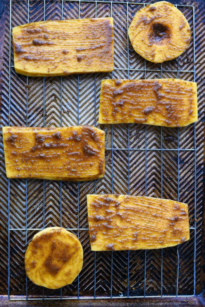 Butternut squash steaks on a baking sheet covered in a spice marinade prior to baking