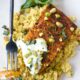 A roasted butternut squash steak with yogurt sauce, pistachios and basil over a bed of couscous and a fork showing a piece cut off