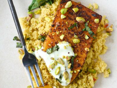 A roasted butternut squash steak over a bed of couscous with yogurt sauce, pistachios and basil