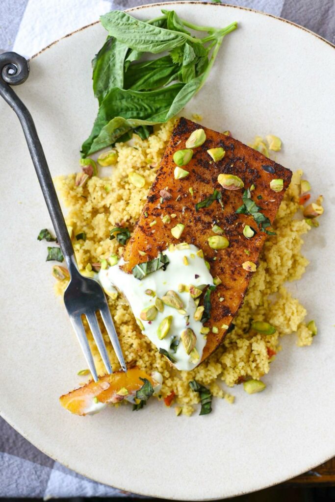 A roasted butternut squash steak over a bed of couscous with yogurt sauce, pistachios and basil