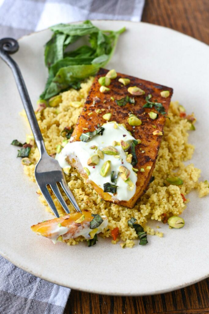 A roasted butternut squash steak on a plate with a piece cut off to show the yellow inside