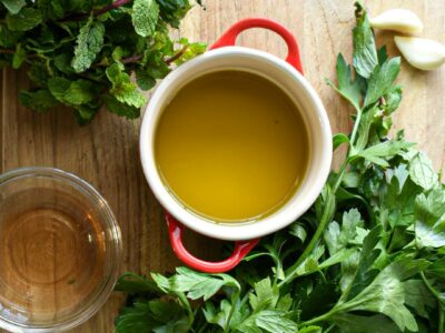 A wooden cutting board with a small bowl of olive oil, salt, red pepper flakes, garlic, vinegar, parsley, and mint