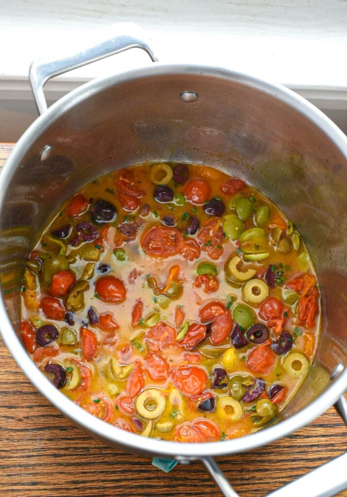 cod baked with tomatoes A large stainless steel pot filled with cherry tomatoes and green and black olives cooked in a white wine and lemon sauce