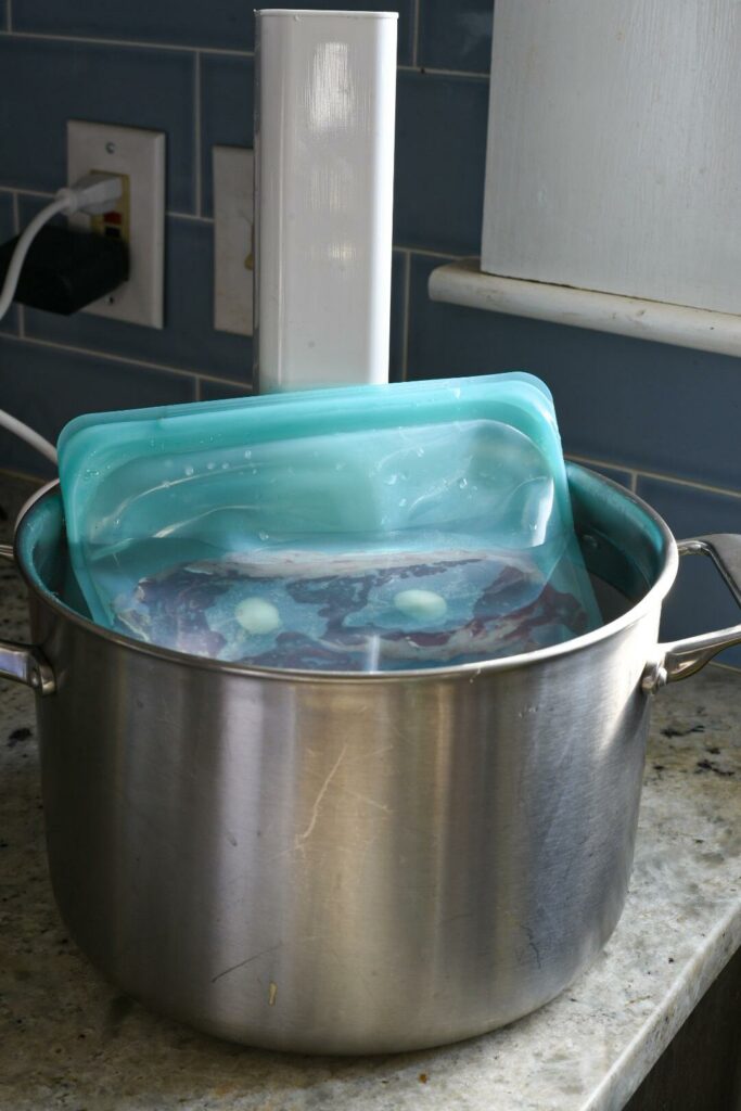 A blue bag in a large pot filled with water and a sous vide machine