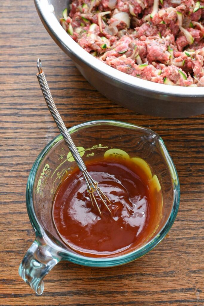 A glass measuring cup filled with ketchup mixture for meatloaf