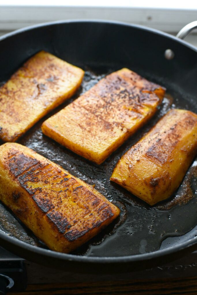 Roasted butternut squash steaks being pan seared in a nonstick skillet