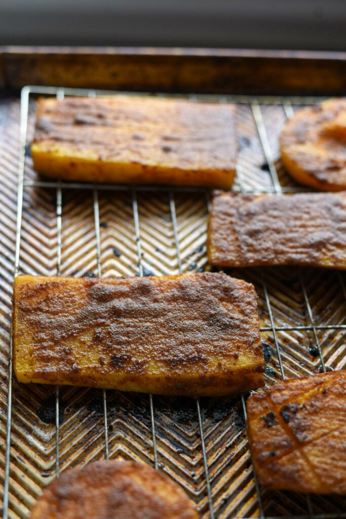 Roasted butternut squash steaks on a wire rimmed baking sheet with a spice marinade on them