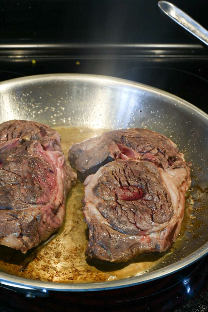 Sous vide steak being flash seared in a stainless steel pan