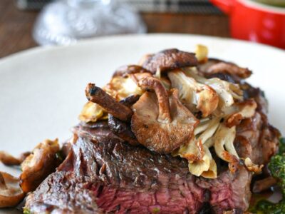 A cooked sous vide sirloin steak cut into to see the medium rare pink inside, topped with wild mushrooms and chimichurri sauce