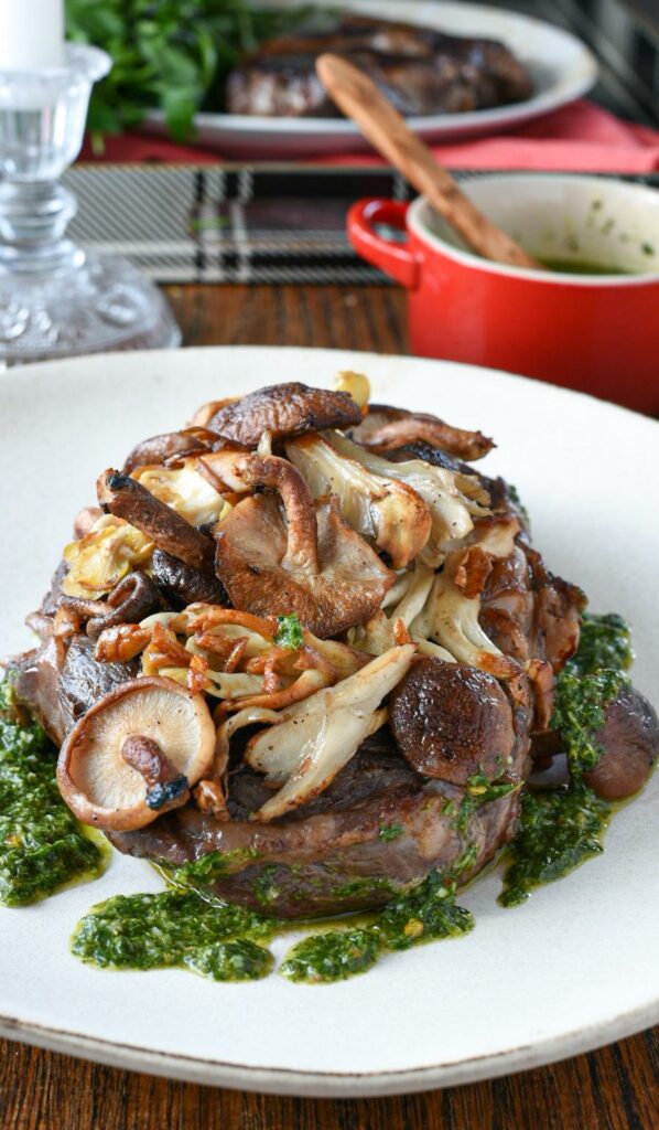 A cooked sous vide sirloin steak topped with sauteed wild mushrooms and bright green chimichurri sauce