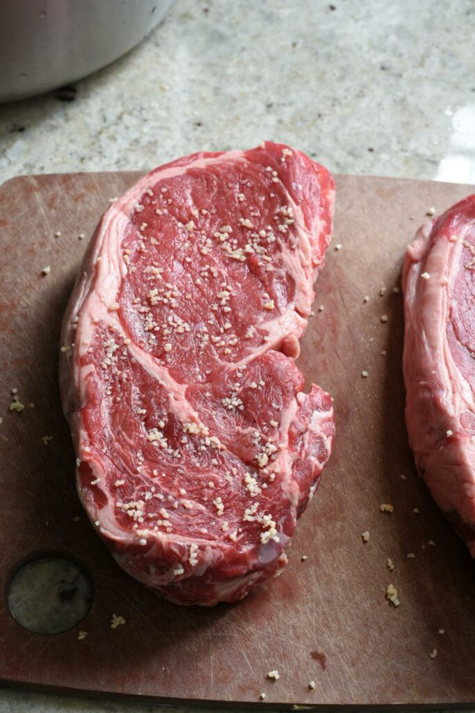 Bright red raw sirloin steaks on a cutting board sprinkled with salt