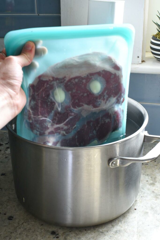 A hand holding a stasher bag filled with sous vide sirloin steak going into a pot
