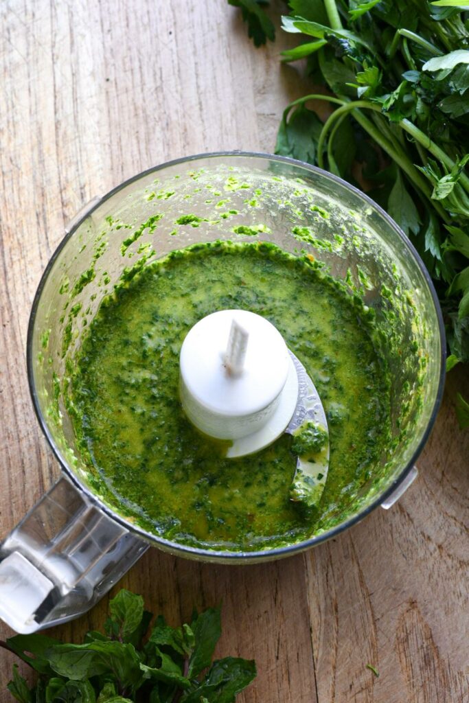 A food processor filled with bright green chimichurri sauce on a wooden board
