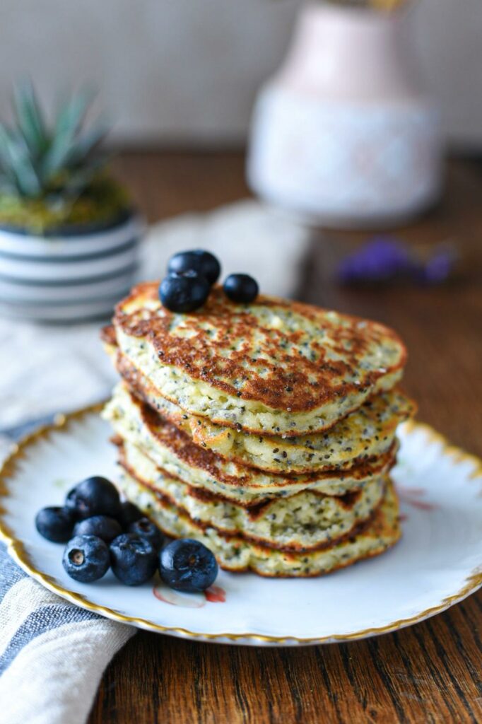 A stack of almond flour banana pancakes on a gold rimmed plate with blueberries on top