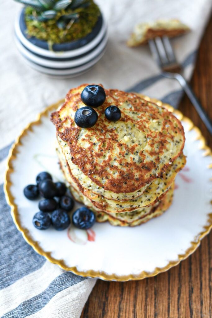 An overhead stack of almond flour banana pancakes speckled with chia seeds on a gold rimmed plate
