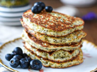 A close up image of a stack of banana almond flour pancakes on a gold rimmed plate with blueberries