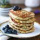 A close up image of a stack of banana almond flour pancakes on a gold rimmed plate with blueberries