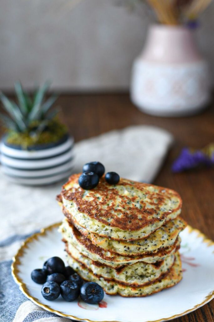 A stack of almond flour banana pancakes with blueberries on top with a plant in the background