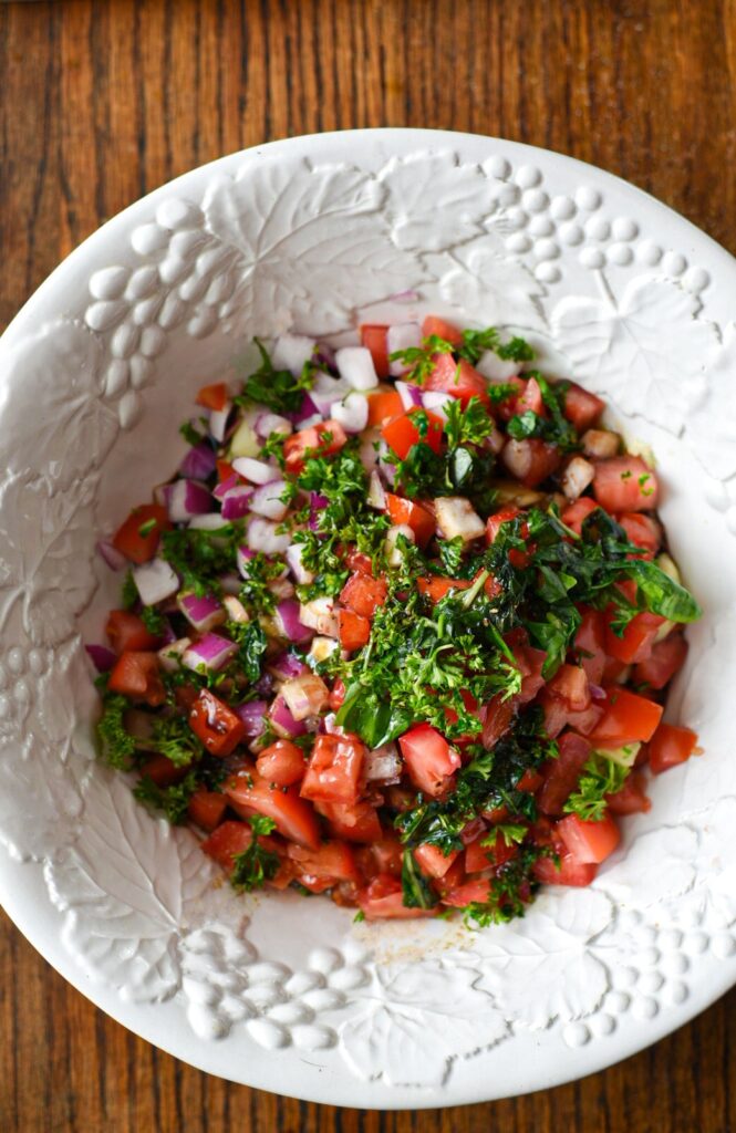 The ingredients for cucumber tomato balsamic salad in a large white bowl with fresh herbs on top, ready to be mixed together.