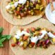 Mediterranean baked fish tacos on a wooden board topped with cucumber tomato balsamic salad and a white lemon garlic yogurt sauce