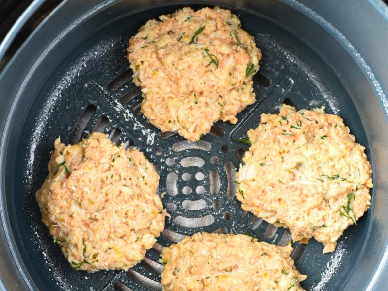 Four raw crab cakes in air fryer before being air fried