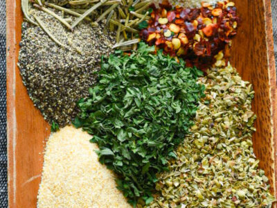 A close up of the spices used for spaghetti seasoning in a wooden bowl prior to being mixed.