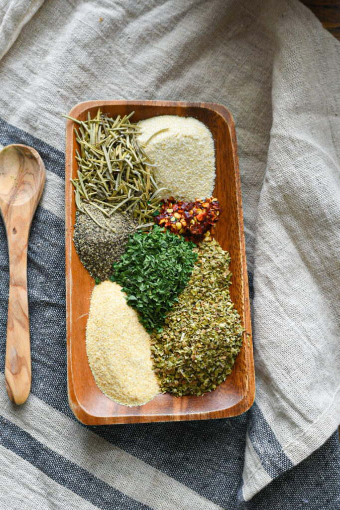 A small rectangular wooden dish filled with spaghetti seasoning spices on top of a grey tea towel.