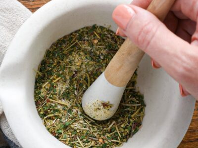 A hand using a mortar and pestle to grind mediterranean diet spices.