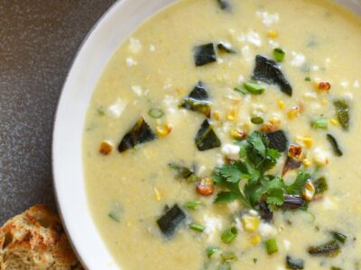 A bowl of yellow poblano corn chowder topped with cilantro and next to a piece of toasted sourdough bread