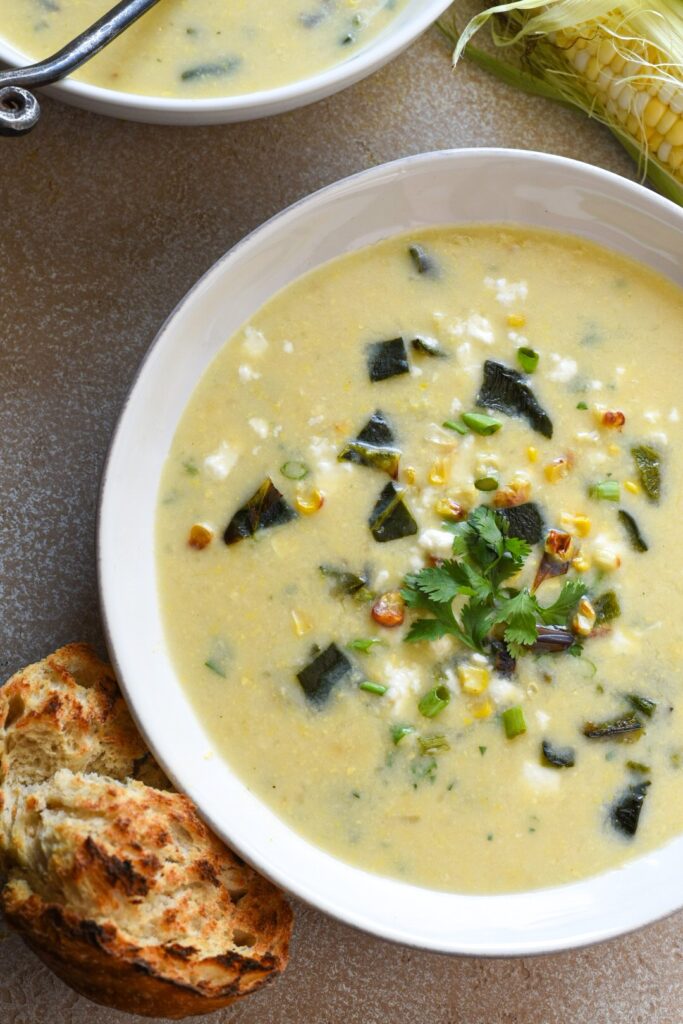 A bowl of yellow poblano corn chowder topped with cilantro and next to a piece of toasted sourdough bread