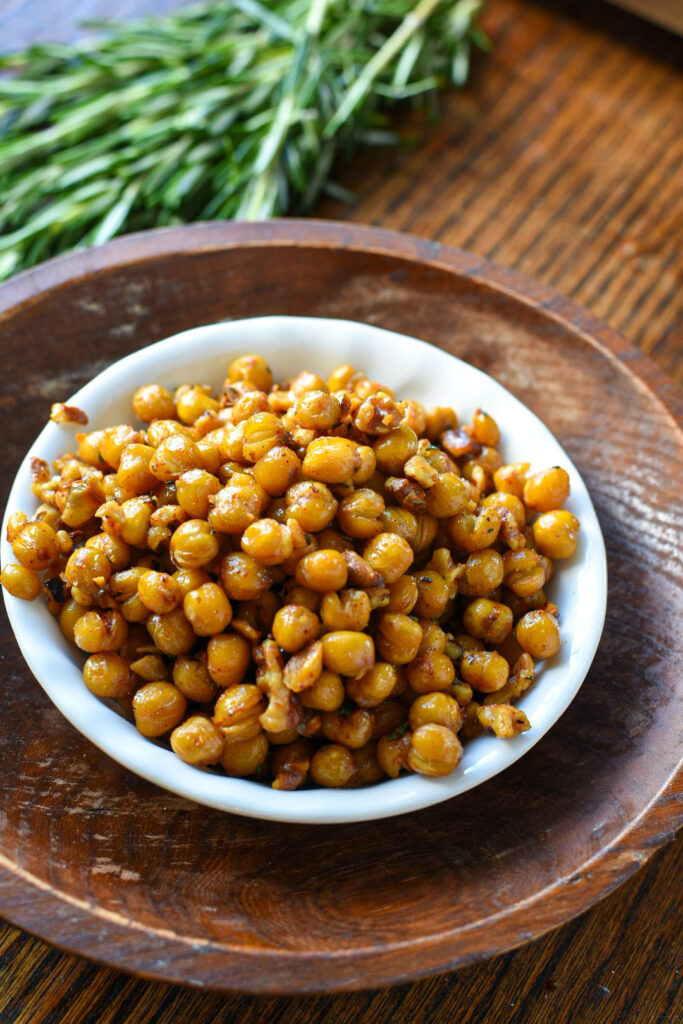 A small white bowl filled with rosemary roasted chickpeas and walnuts recipe, inside of a larger wooden bowl