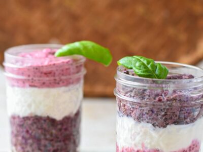 Two glass mason jars filled with red and purple chia seed pudding and white yogurt in a layering pattern
