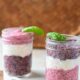 Two glass mason jars filled with red and purple chia seed pudding and white yogurt in a layering pattern