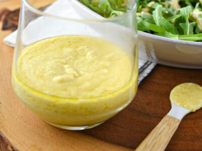 Creamy parmesan vinaigrette in a glass container next to a salad of arugula