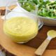 Creamy parmesan vinaigrette in a glass container next to a salad of arugula