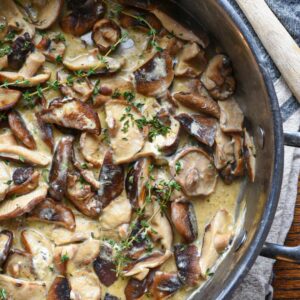 A large stainless steel pan filled with creamy mushrooms in a goat cheese sauce sprinkled with thyme