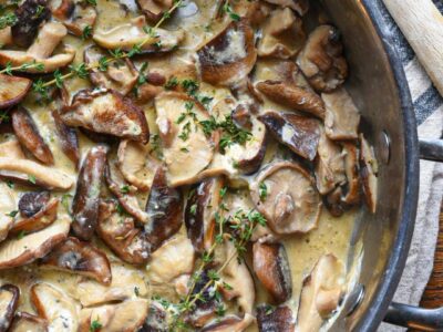 A large stainless steel pan filled with creamy mushrooms in a goat cheese sauce sprinkled with thyme
