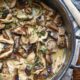 A large stainless steel pan filled with creamy mushrooms in a goat cheese sauce sprinkled with thyme