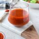 A clear glass filled with bright red harissa vinaigrette with a salad in the background