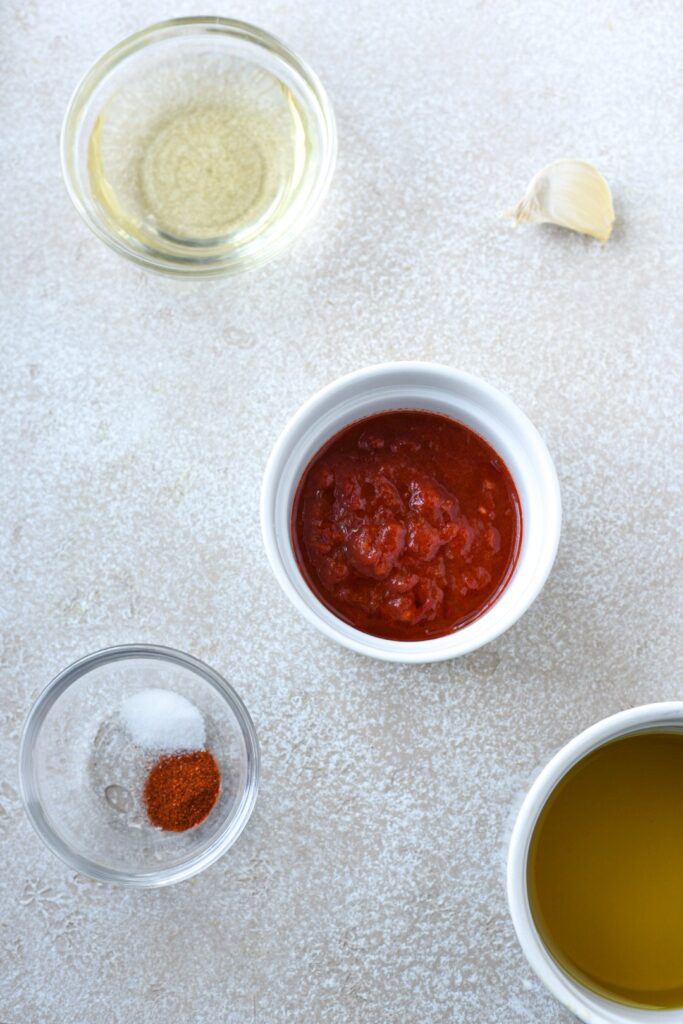 An overhead shot of the ingredients needed to make harissa vinaigrette like garlic, olive oil, vinegar, spices and harissa paste