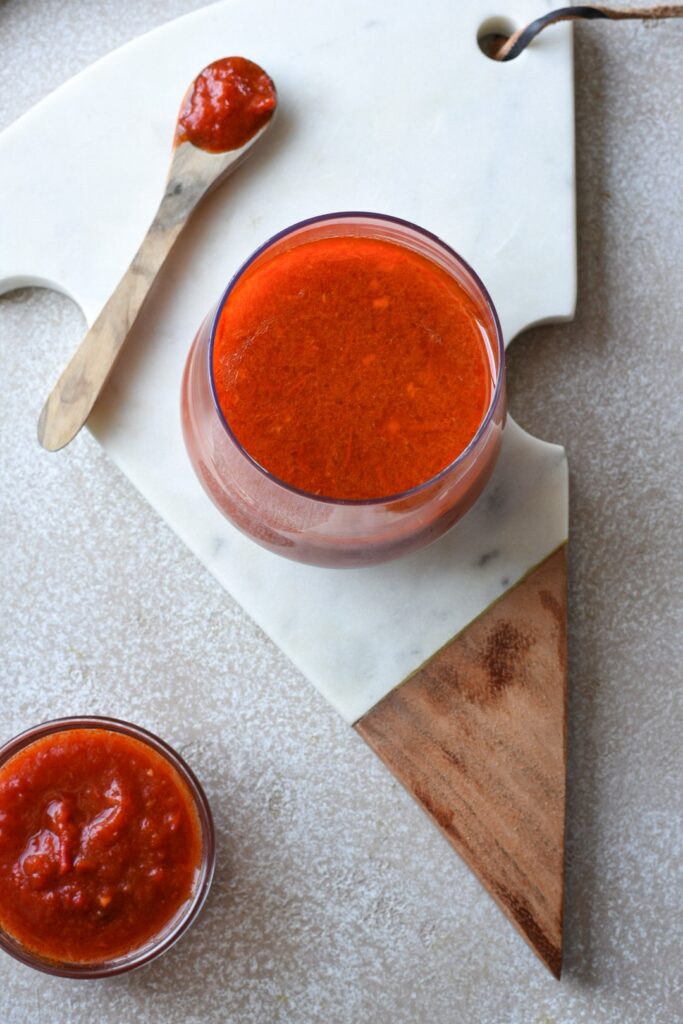 An overhead close up image of harissa dressing with a wooden spoon and an bowl of harissa sauce next to it 