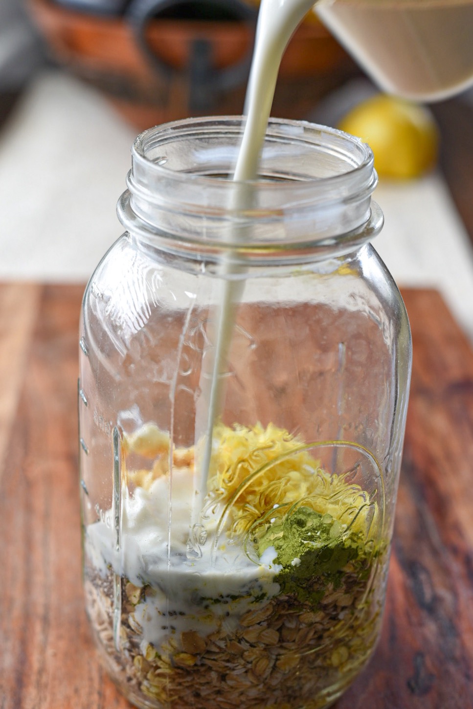 A large glass mason jar filled with matcha overnight oats with milk being poured into the jar
