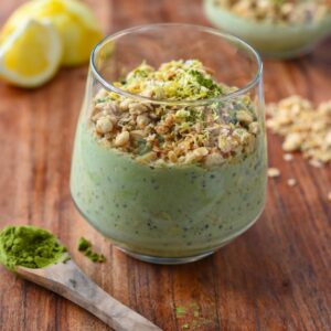 Green matcha overnight oats in a glass cup topped with granola and lemon zest on a wooden cutting board