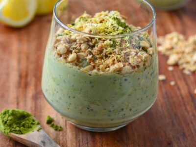 Green matcha overnight oats in a glass cup topped with granola and lemon zest on a wooden cutting board